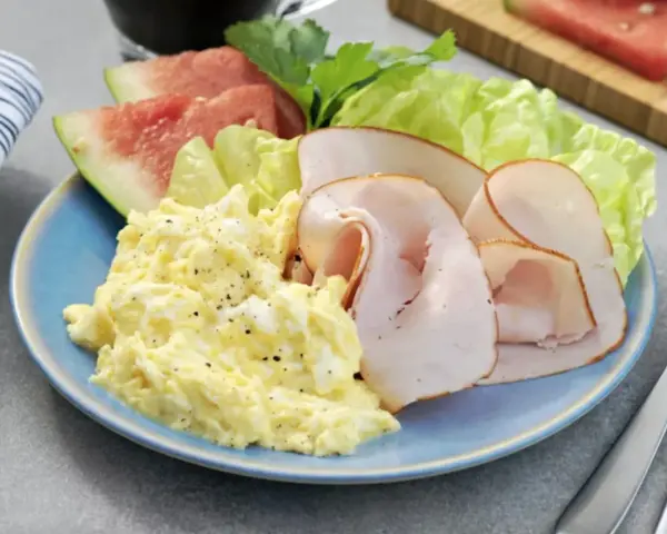 En blå tallrik med äggröra, kalkonpålägg, vattenmelon och sallad. En perfekt 5:2 frukost för en hälsosam start.