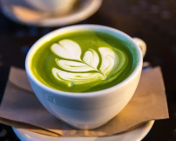 En vit kopp med grön matcha latte, dekorerad med mjölkskum. Även om det är gott, kan man uppleva matcha te biverkningar om man dricker för mycket.