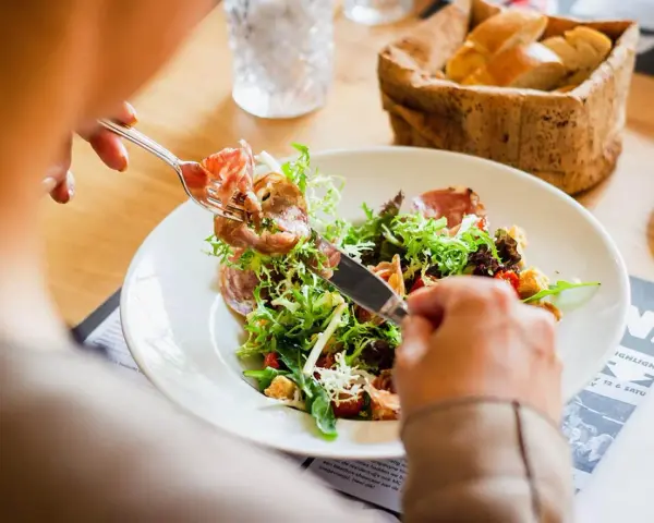 En person äter en sallad med skinka, en del av en 800 kcal diet. Brödkorg i bakgrunden.