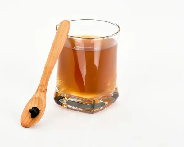 En träsked med shilajit bredvid ett glas med en brun dryck. Var medveten om potentiella shilajit biverkningar.
