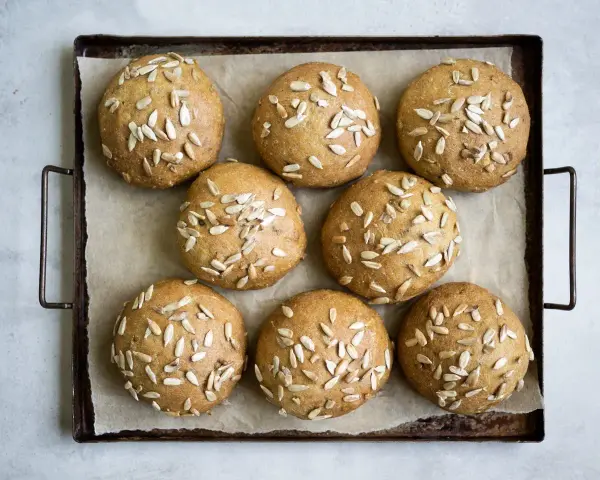 Nio gyllene glutenfria morotsfrallor toppade med solrosfrön ligger på en plåt.