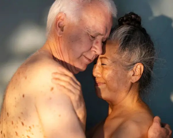 Ett äldre par omfamnar varandra ömt, deras ansikten nära varandra. Ljuset faller mjukt över dem och framhäver deras hud. Kärlek och närhet lyser igenom, en påminnelse om att bra sex kan finnas i alla åldrar.