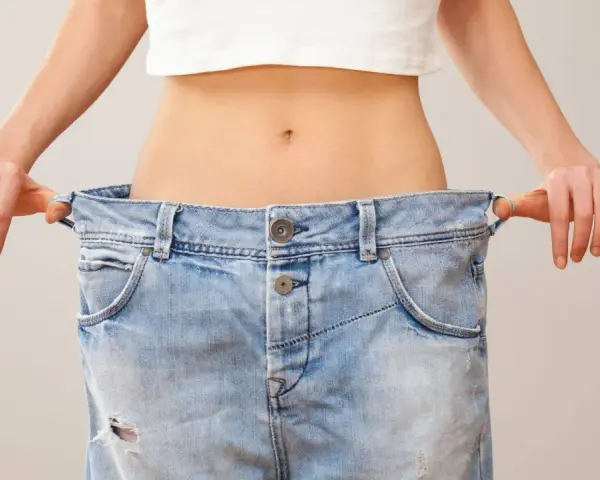 En person visar upp sina jeans som är alldeles för stora, ett tydligt tecken på att hon lyckats gå ner 10 kg.