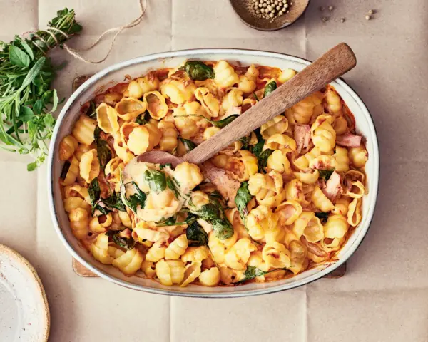 En krämig pastarätt med spenat och lax, perfekt för nyttiga recept. En träsked lyfter upp en portion ur ugnsformen.