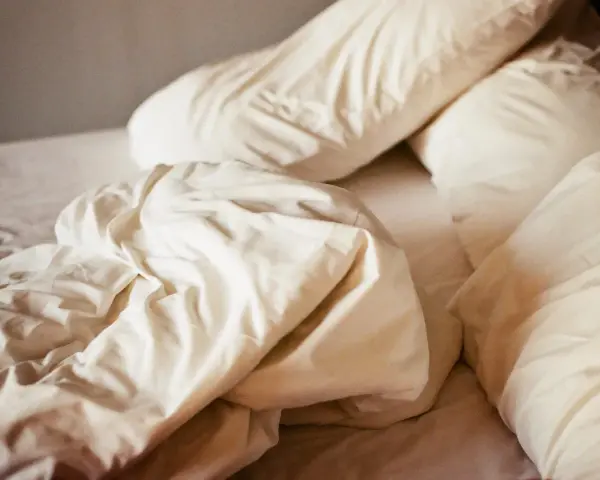 Ovanpå en bädd med vita lakan och kuddar, en påminnelse om att sömnmedel som melatonin kan ge biverkningar.