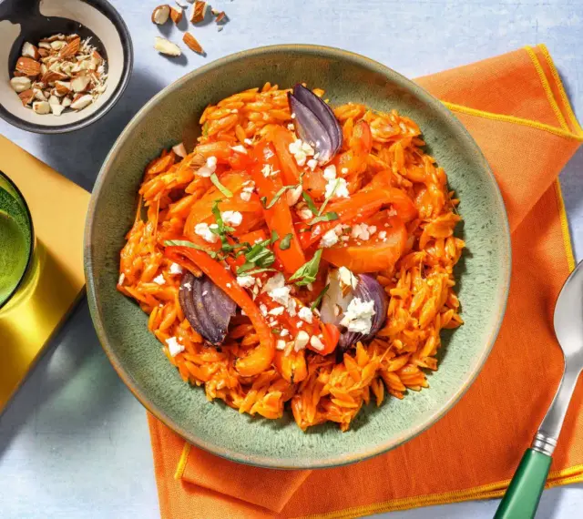 En skål med orzopasta med rostade grönsaker och fetaost, ett härligt medelhavskost recept. Toppad med mandlar och färska örter.