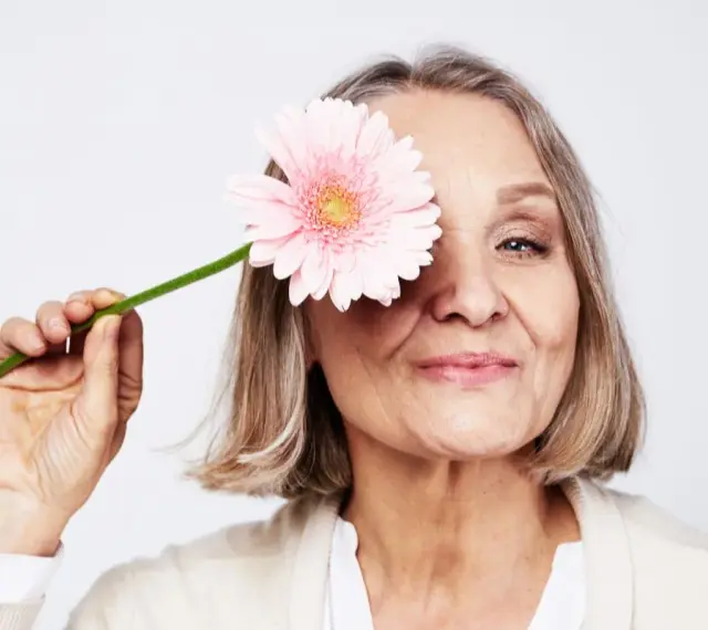 En kvinna med en rosa blomma framför ögat. Hon ler mjukt, en symbol för att hon mår bra och kanske vill gå ner i vikt under klimakteriet.