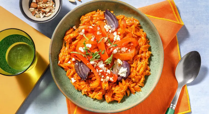 En skål med orzopasta med rostade grönsaker och fetaost, ett härligt medelhavskost recept. Toppad med mandlar och färska örter.