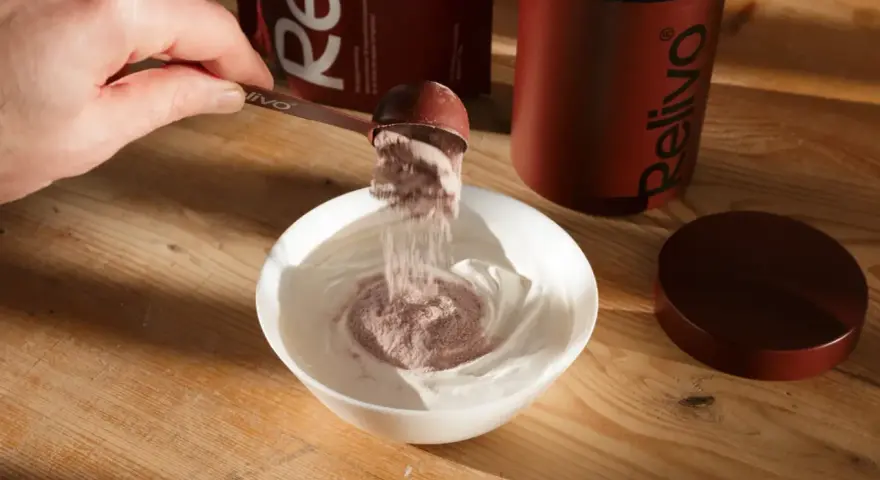 Pulver från en skopa blandas i en skål med yoghurt. En burk och förpackning från Relivo syns i bakgrunden. Perfekt för att dricka mer!