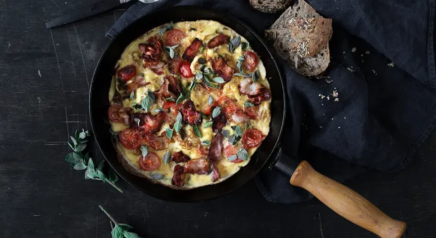 En saftig omelett med knaprigt bacon och körsbärstomater, serverad i en gjutjärnsstekpanna. Perfekt för en härlig frukost eller brunch.