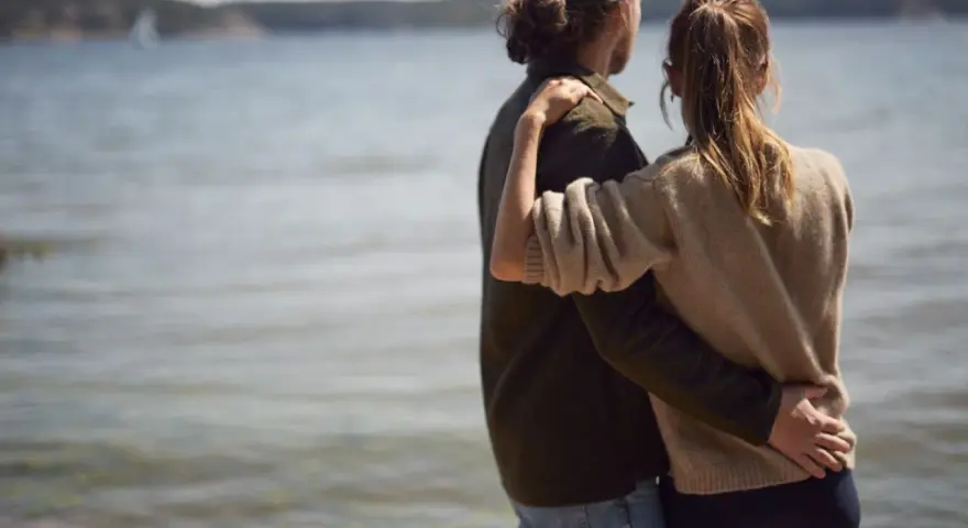 Par vid vattnet, en kvinna i sin bästa ålder med sexlust, omfamnar sin partner.