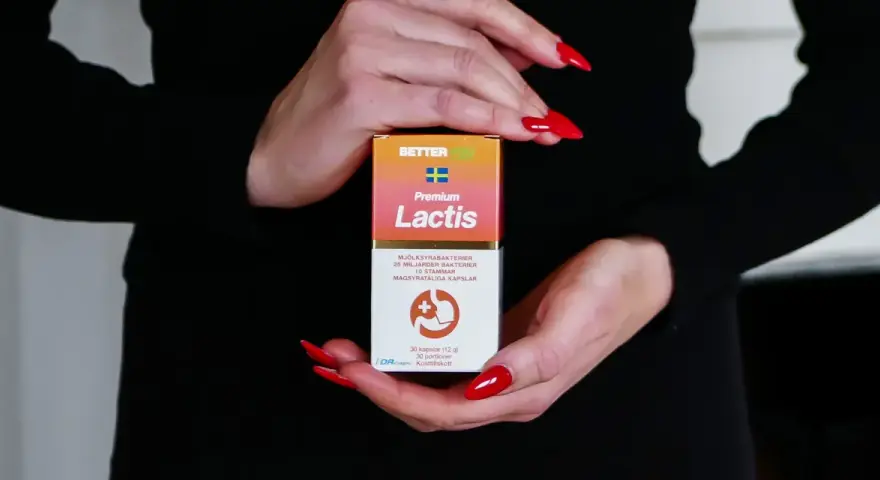 Händer med röda naglar håller en kartong med probiotika för IBS. Lactis innehåller mjölksyrabakterier för magen.
