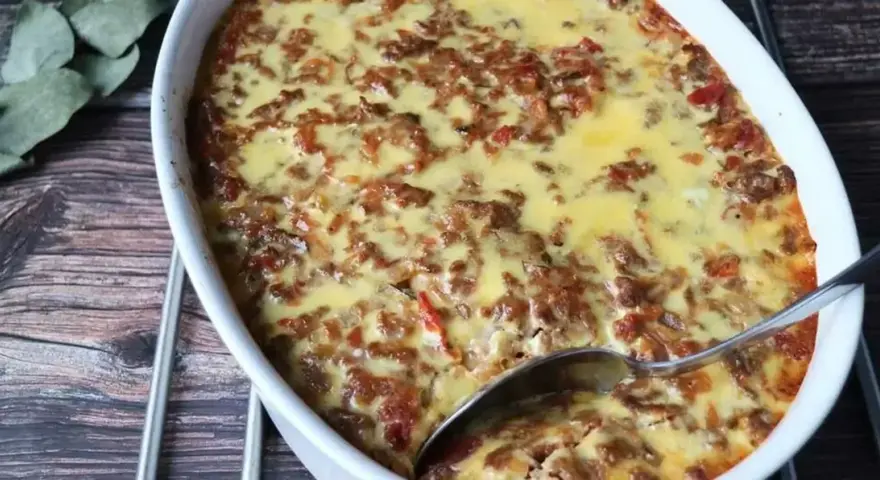 LCHF moussaka i ugnsform, gyllene och bubblande. En sked är redo att servera denna läckra, köttfärsfyllda gratäng.