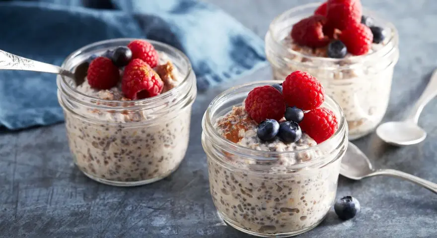 Tre burkar med overnight oats recept, toppade med hallon och blåbär. En perfekt frukost att förbereda kvällen innan.