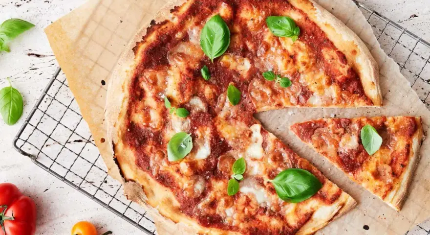 En läcker pizza med tomatsås, ost och färsk basilika. En bit är bortskuren, perfekt för att njuta av dess kalorier.