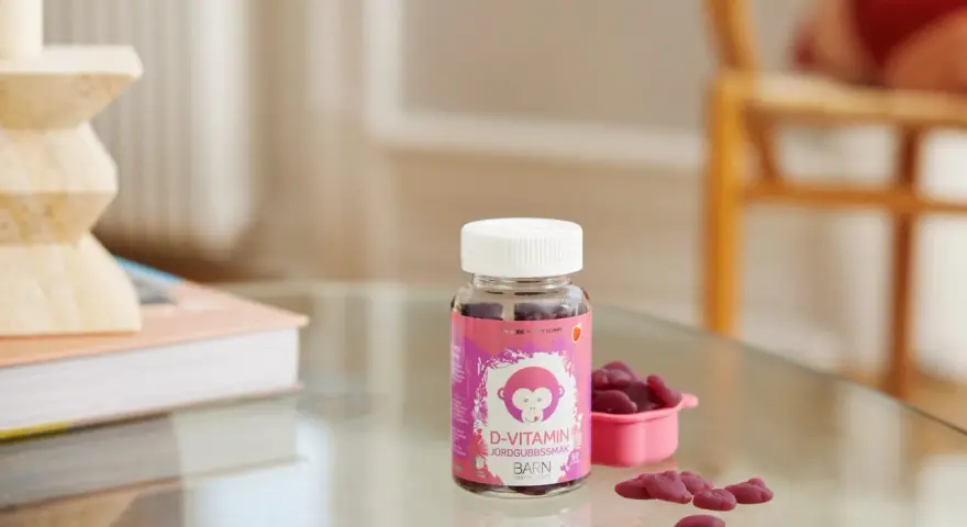 D-vitamin jordgubbssmak för barn. En burk med rosa etikett och en apa, bredvid en rosa skål med hjärtformade gummies.