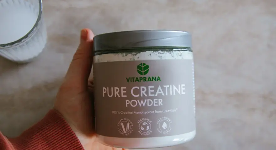 En hand håller en burk med VitaPrana Pure Creatine Powder. Kan vara ett bra tillskott för att hantera energi under klimakteriet.