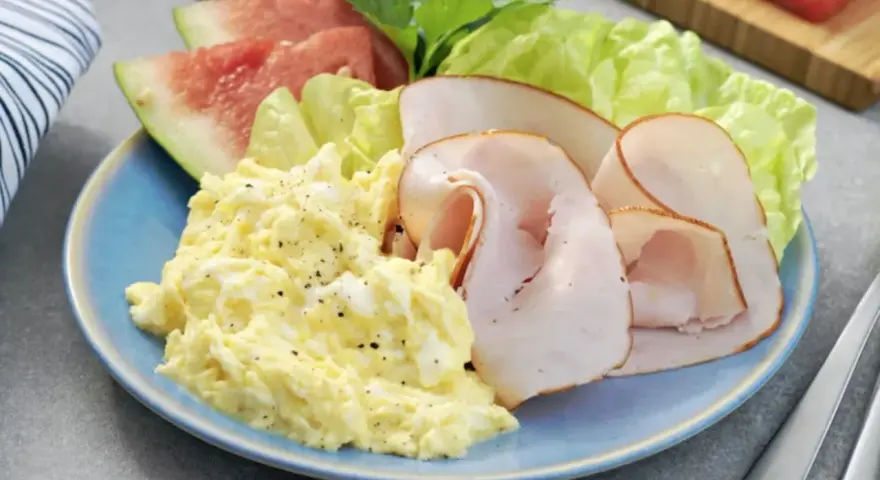 En blå tallrik med äggröra, kalkonpålägg, vattenmelon och sallad. En perfekt 5:2 frukost för en hälsosam start.