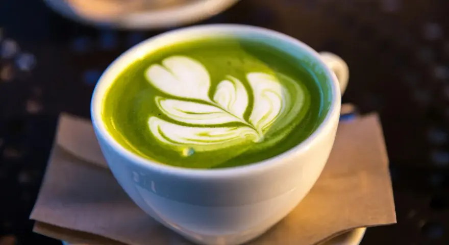 En vit kopp med grön matcha latte, dekorerad med mjölkskum. Även om det är gott, kan man uppleva matcha te biverkningar om man dricker för mycket.