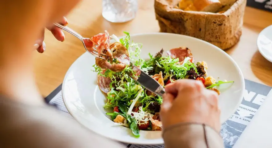 En person äter en sallad med skinka, en del av en 800 kcal diet. Brödkorg i bakgrunden.