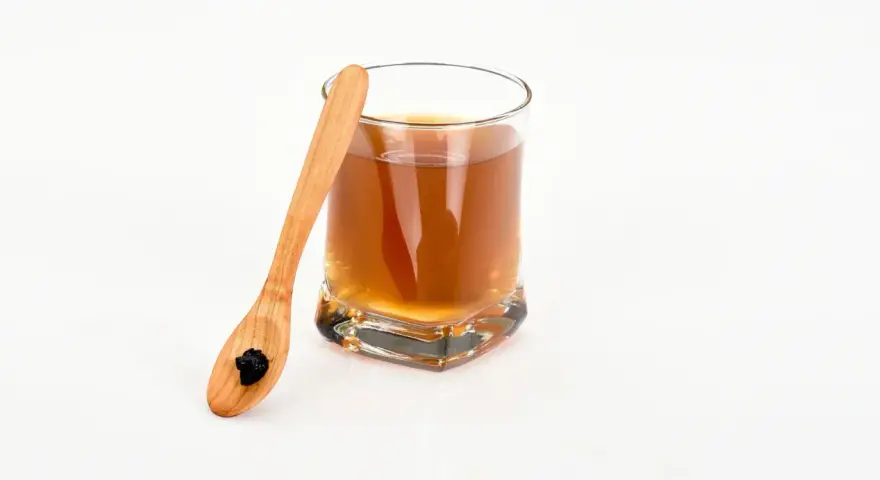 En träsked med shilajit bredvid ett glas med en brun dryck. Var medveten om potentiella shilajit biverkningar.
