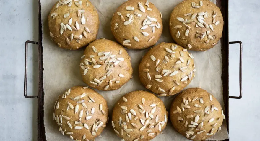 Nio gyllene glutenfria morotsfrallor toppade med solrosfrön ligger på en plåt.