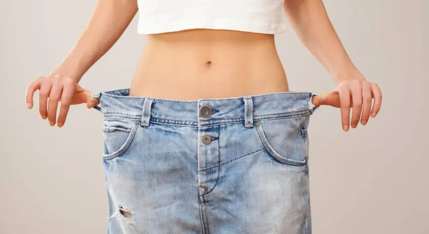En person visar upp sina jeans som är alldeles för stora, ett tydligt tecken på att hon lyckats gå ner 10 kg.