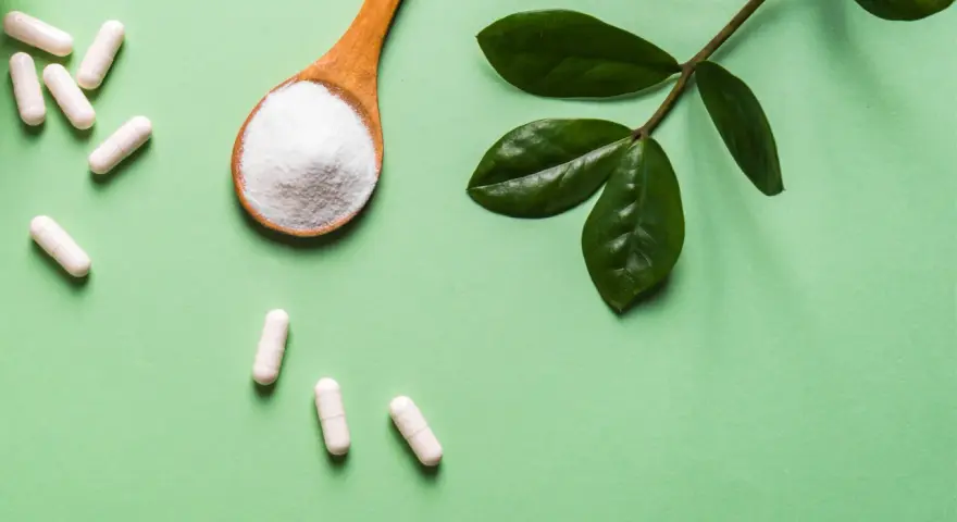 Vita kapslar och en sked med vitt pulver, bredvid gröna blad. Information om moringa biverkningar kan vara relevant.