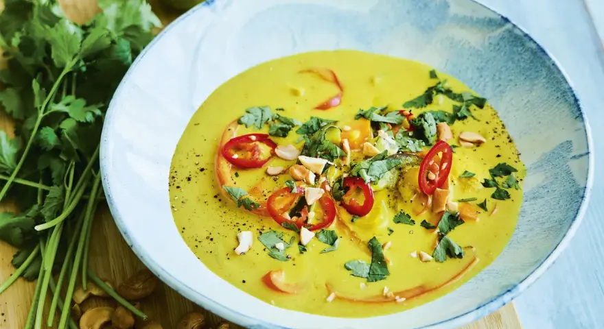 En krämig kycklingpaj med curry, toppad med chili, koriander och cashewnötter. Serveras i en vacker blåvit skål.