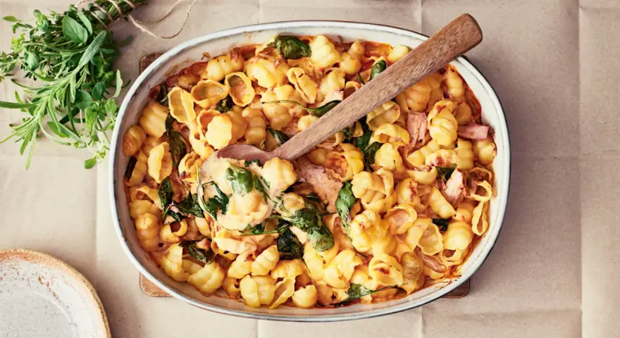 En krämig pastarätt med spenat och lax, perfekt för nyttiga recept. En träsked lyfter upp en portion ur ugnsformen.