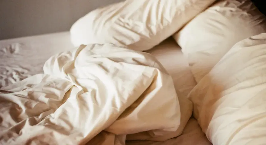 Ovanpå en bädd med vita lakan och kuddar, en påminnelse om att sömnmedel som melatonin kan ge biverkningar.