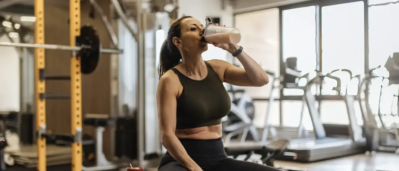 Kvinna dricker proteinshake i gymmet. Hon k&auml;nner sig stark och energisk, trots klimakteriet, och anv&auml;nder kreatin f&ouml;r att boosta sina resultat.