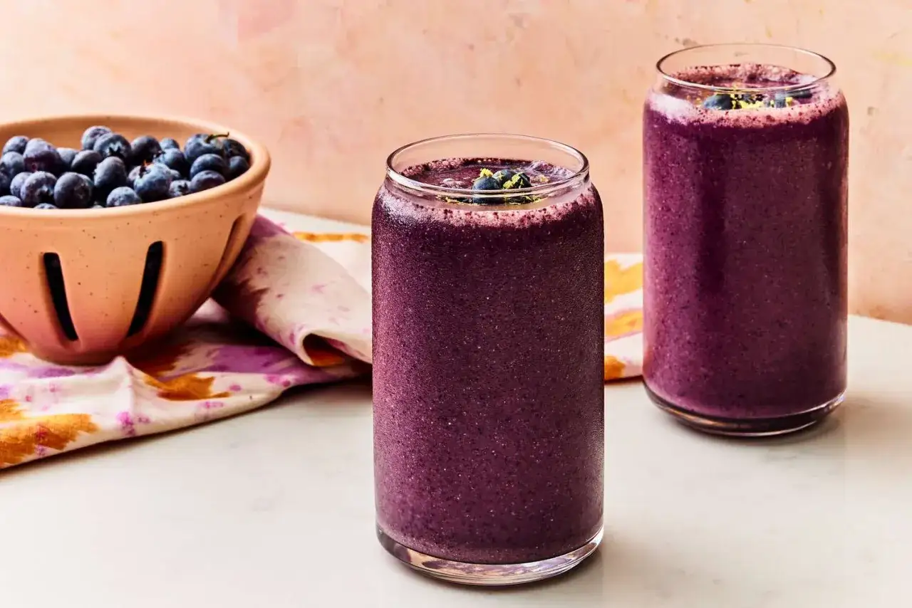Tv&aring; glas med lila smoothie, perfekt f&ouml;r en smoothie viktnedg&aring;ng. En sk&aring;l med bl&aring;b&auml;r bredvid.
