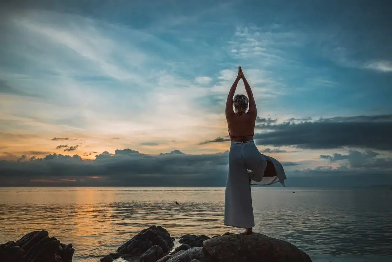 Kvinna i solnedg&aring;ng p&aring; stranden, balanserar i yogapose. En inspiration f&ouml;r att g&aring; ner i vikt efter 50.