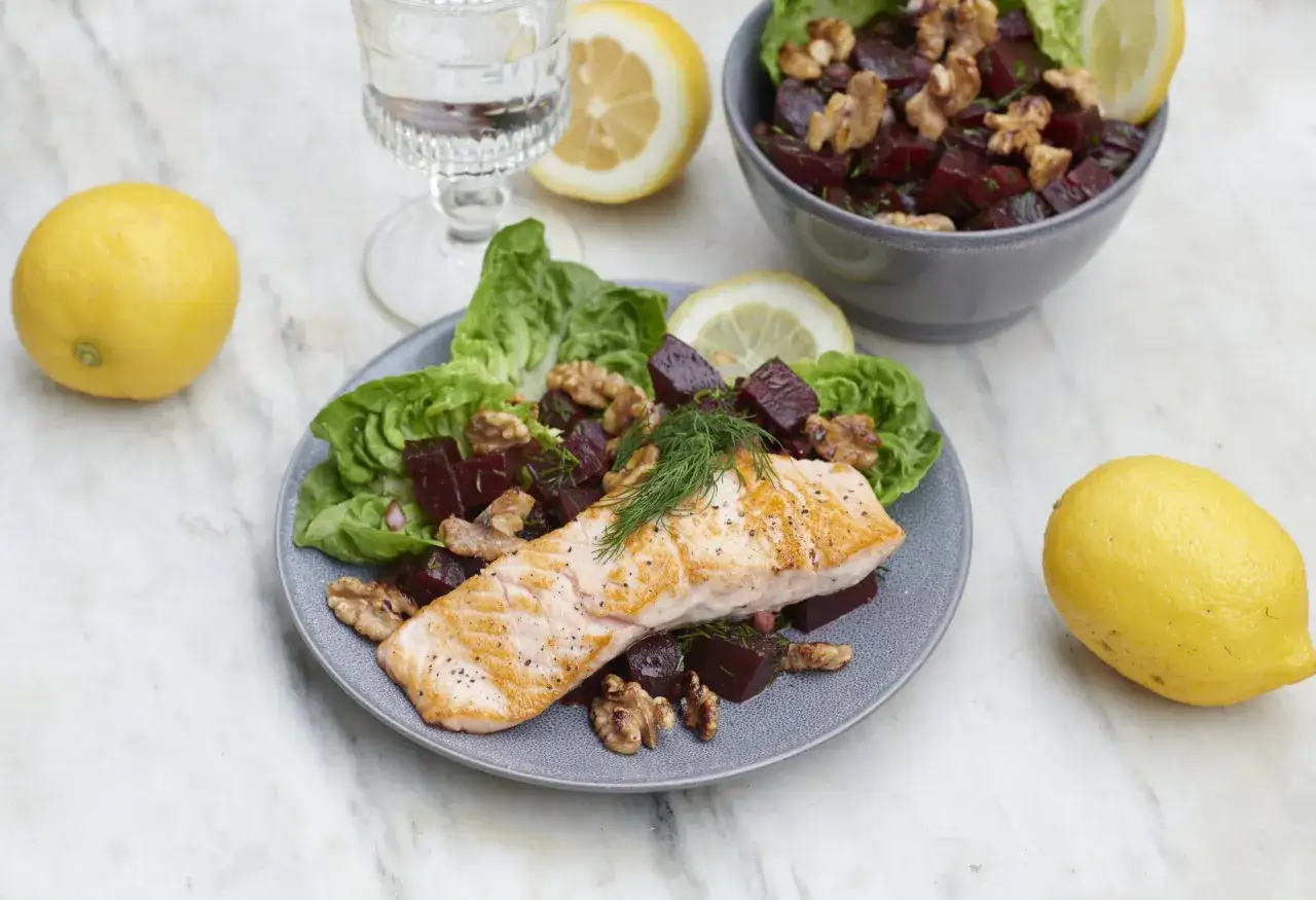 En vacker tallrik med lax, r&ouml;dbetor, valn&ouml;tter och sallad, inspirerad av Ulrika Davidsson recept. Citroner och ett glas vatten full&auml;ndar dukningen.