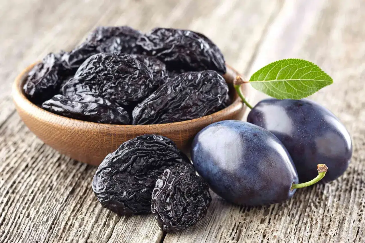 Torkade plommon i en sk&aring;l och f&auml;rska plommon p&aring; tr&auml;bord. Plommon nyttigt f&ouml;r magen och fullt av vitaminer.