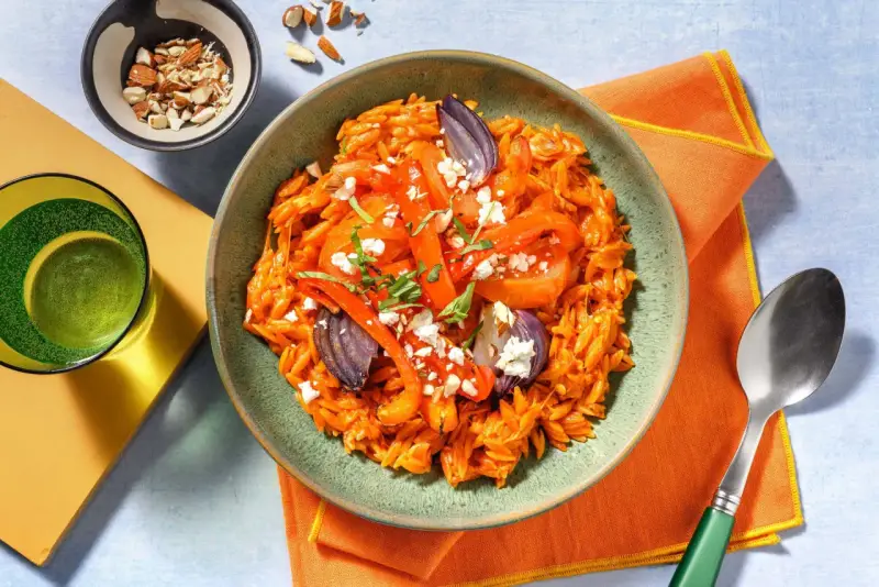 En skål med orzopasta med rostade grönsaker och fetaost, ett härligt medelhavskost recept. Toppad med mandlar och färska örter.