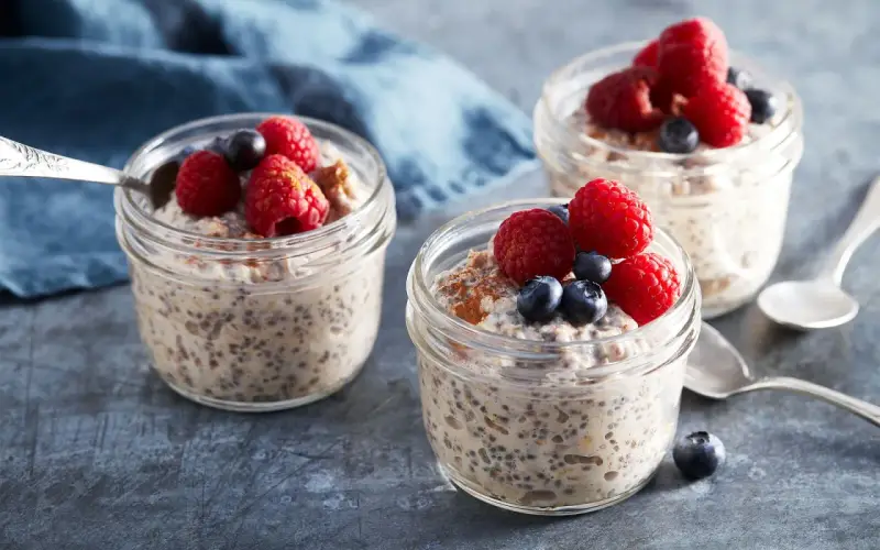 Tre burkar med overnight oats recept, toppade med hallon och blåbär. En perfekt frukost att förbereda kvällen innan.