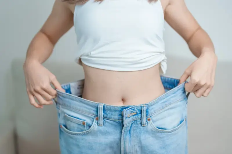 En person visar upp sina för stora jeans, ett tydligt tecken på att de lyckats gå ner i vikt.