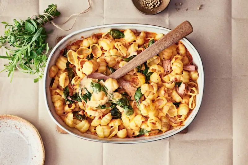 En krämig pastarätt med spenat och lax, perfekt för nyttiga recept. En träsked lyfter upp en portion ur ugnsformen.