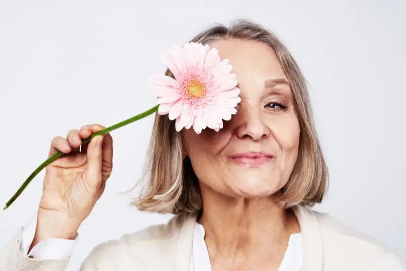 En kvinna med en rosa blomma framför ögat. Hon ler mjukt, en symbol för att hon mår bra och kanske vill gå ner i vikt under klimakteriet.