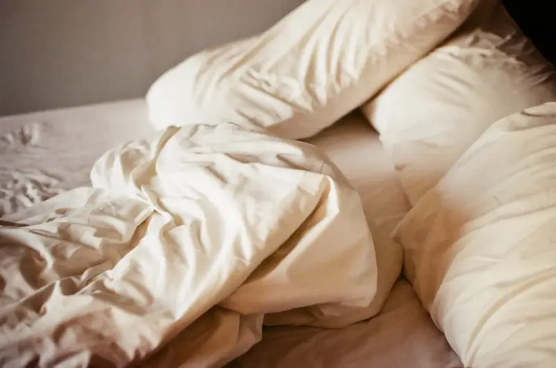 Ovanpå en bädd med vita lakan och kuddar, en påminnelse om att sömnmedel som melatonin kan ge biverkningar.